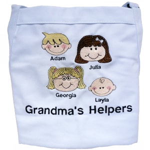 Puede incluir: Un delantal azul claro con el texto "Grandma's Helpers" bordado en la parte inferior. Cuatro caras de dibujos animados están bordadas encima del texto, cada una con un nombre debajo: Adam, Julia, Georgia y Layla.