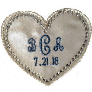 May include: White satin heart-shaped patch with a blue embroidered monogram "BCA" and the date "7.21.18" surrounded by a border of clear rhinestones.