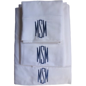 Könnte beinhalten: Ein Set aus drei weißen Kissenbezügen mit einem dunkelblauen Monogramm der Buchstaben "MSM", das auf jeden gestickt ist.