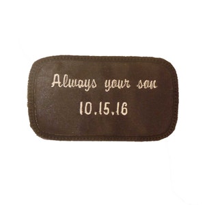 May include: A brown rectangular patch with white embroidered text that reads "Always your son 10.15.16".