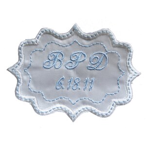 May include: White embroidered fabric label with a scalloped edge. The label has the initials "BPD" and the date "6.18.11" embroidered in blue thread.