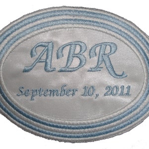 May include: White oval satin patch with blue embroidered edging. The patch has the initials "ABR" and the date "September 10, 2011" embroidered in blue.