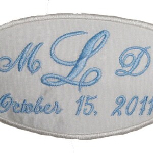 May include: White oval fabric patch with blue embroidered lettering. The lettering reads "M & L" with a stylized ampersand and "October 15, 2011".