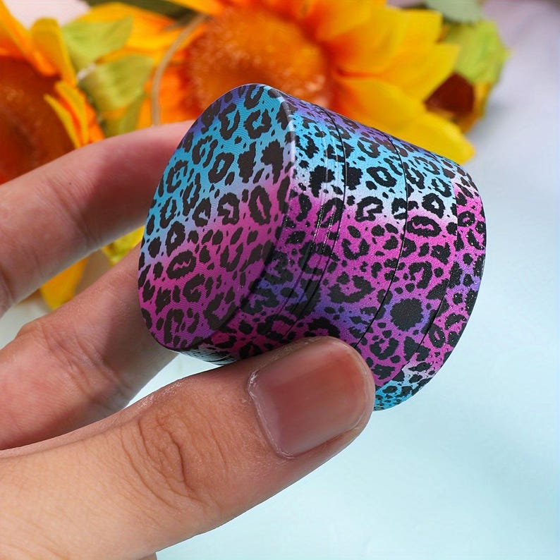 Op de afbeelding: Een veelkleurige grinder met een luipaardprint. De grinder is gemaakt van metaal en heeft een blauwe, roze en paarse kleurstelling.