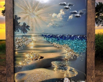May include: A framed resin art piece depicting a beach scene with a sunset, palm trees, and seashells. The artwork features a blue and turquoise background with glitter accents.