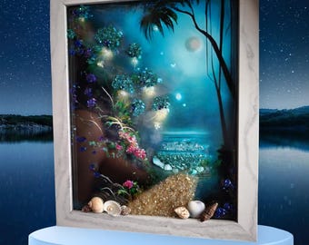 May include: A framed mixed media artwork depicting a nighttime seascape with a full moon, palm trees, and glowing blue flowers. The artwork is set in a white frame and includes textured elements like sand, shells, and glitter.