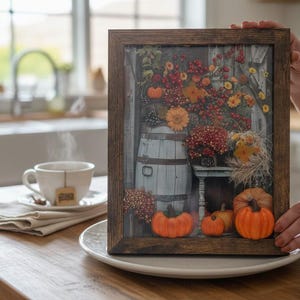 Könnte beinhalten: Ein rechteckiger Holzrahmen mit einem Druck einer rustikalen Herbstszene. Das Bild zeigt ein hellblaues Holzfass, orangefarbene Kürbisse und ein lebhaftes Arrangement aus roten Beeren und gelben Blumen vor einem verwitterten grauen Hintergrund.