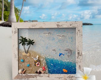 May include: A framed resin art piece depicting a beach scene with palm trees, seagulls, dolphins, seashells, and a life preserver. The frame is white with a distressed finish.