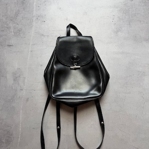 Puede incluir: Mochila de cuero negro con cierre de solapa y herrajes plateados. La bolsa tiene correas ajustables para los hombros y un asa superior. La mochila se muestra sobre un fondo gris.