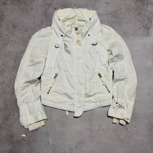 May include: Cream-coloured jacket with a high collar, zip closure, and decorative stitching. It has two zipped front pockets and embroidered floral details on the sleeves. The jacket features a button closure and strap detail.