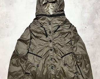 May include: A hooded olive green jacket with a button-up front and black trim. The jacket has a cinched waist and pockets. The hood is lined with a shiny, metallic fabric. The jacket is made of a lightweight, possibly water-resistant material.
