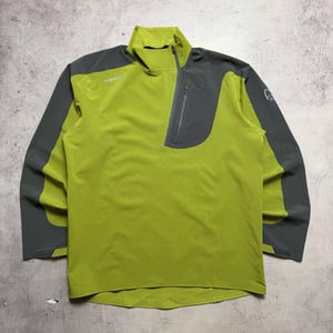 May include: A lime green and gray long-sleeved athletic top. The top features a quarter-zip closure, a small chest pocket, and the brand name "NORRØNA" printed on the chest. The sleeves and upper chest are gray.