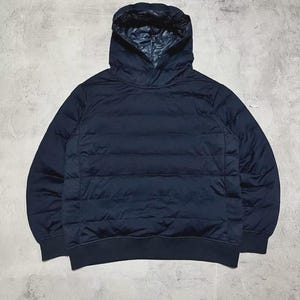 May include: A navy blue hooded sweatshirt with a quilted front panel. The hood has a contrasting dark blue lining. The sweatshirt has a ribbed hem and cuffs. The garment is made of a soft, possibly padded material.