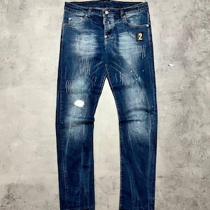May include: Blue denim jeans with distressed details, including a ripped knee and paint splatter accents. The jeans feature a classic five-pocket design and a small patch with the number "2".
