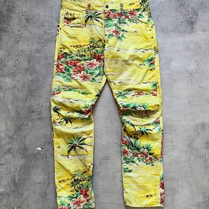 Puede incluir: Pantalones vaqueros amarillos con estampado floral tropical y palmeras. Los pantalones tienen un corte de pierna recta y cierre de botón y cremallera. El estampado floral incluye flores rojas, rosas y verdes.