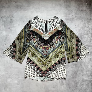 May include: A patterned blouse with a V-neck and wide sleeves. The top features a mix of colors including black, white, green, and red, with an intricate paisley and geometric design. The blouse is made of a lightweight fabric.