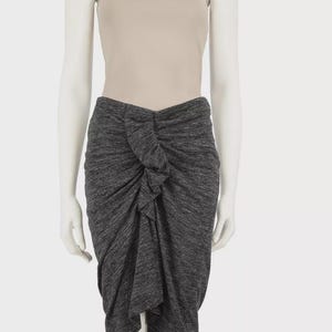 May include: A gray, textured skirt with a knot detail at the waist. The skirt has an asymmetrical hemline and is paired with a beige camisole top. The fabric appears to be a soft knit material.