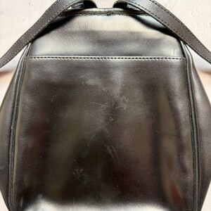 May include: A black leather backpack with adjustable straps. The backpack has a small pocket on the back and silver-colored hardware. The leather shows some wear and tear, with visible scratches and marks on the surface.