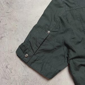 May include: Dark green short-sleeved shirt with a buttoned cuff. The shirt has a classic design with a button on the sleeve and a decorative button near the shoulder. The fabric appears to be a lightweight material.