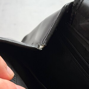 May include: Close-up of a black leather bag with a visible tear at the seam. The bag's interior is also visible, revealing a black fabric lining and a zipper. The image highlights the bag's texture and construction details.
