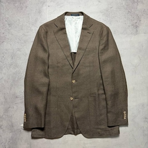 Könnte beinhalten: Ein brauner Blazer mit Zwei-Knopf-Verschluss, zwei Vordertaschen und geknöpften Manschetten. Der Blazer hat ein weißes Futter und ein fallendes Revers. Das Kleidungsstück wird auf einer grauen Oberfläche präsentiert.