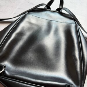 May include: A black, glossy backpack with adjustable straps and a top handle. The bag has a sleek, minimalist design, with a smooth, reflective surface. The backpack appears to be made of a durable material, suitable for everyday use.