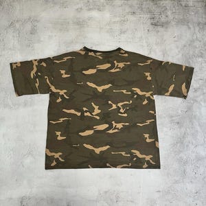 Puede incluir: Camiseta con estampado de camuflaje verde oliva con mangas cortas. La camiseta presenta un patr&oacute;n repetitivo de formas marrones y beige. La camiseta est&aacute; hecha de un material suave y c&oacute;modo.