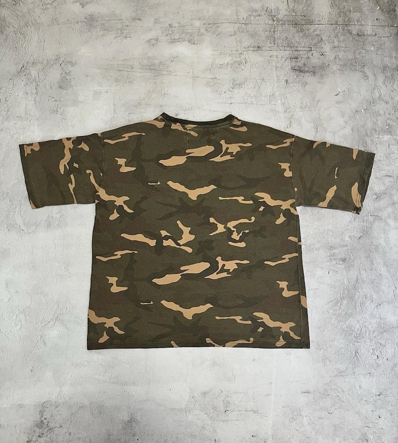 Puede incluir: Camiseta con estampado de camuflaje verde oliva con mangas cortas. La camiseta presenta un patr&oacute;n repetitivo de formas marrones y beige. La camiseta est&aacute; hecha de un material suave y c&oacute;modo.