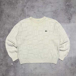 May include: Cream-coloured sweater with a geometric pattern. The long-sleeved knitwear features a crew neck and a small green crocodile logo on the chest. The sweater has a textured design and ribbed cuffs and hem.