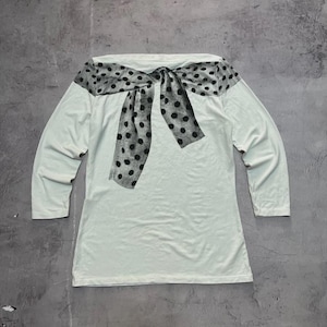 May include: A long-sleeved, off-white top featuring a large, decorative bow. The bow is made of a sheer, gray fabric with black polka dots. The top has a simple, classic design.