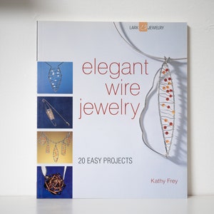 May include: Book cover with the title "elegant wire jewellery" and the subtitle "20 easy projects". The cover features several wire jewellery designs, including a necklace, a pendant, and a brooch. The author is Kathy Frey.