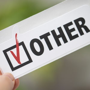 May include: A white sticker with a black tick box and a red tick mark. The text "OTHER" is printed in black letters.