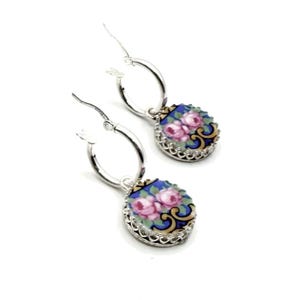 Peut inclure: Une paire de boucles d'oreilles cr&eacute;oles en argent avec des breloques ovales pendantes. Chaque breloque pr&eacute;sente un fond bleu avec un motif floral de roses roses, rehauss&eacute; de volutes dor&eacute;es et d'une bordure en m&eacute;tal argent&eacute; festonn&eacute;.