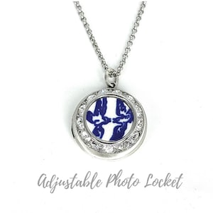 May include: A silver-coloured adjustable photo locket necklace. The round pendant has a blue and white design, encircled by clear crystals. The necklace features a delicate chain.