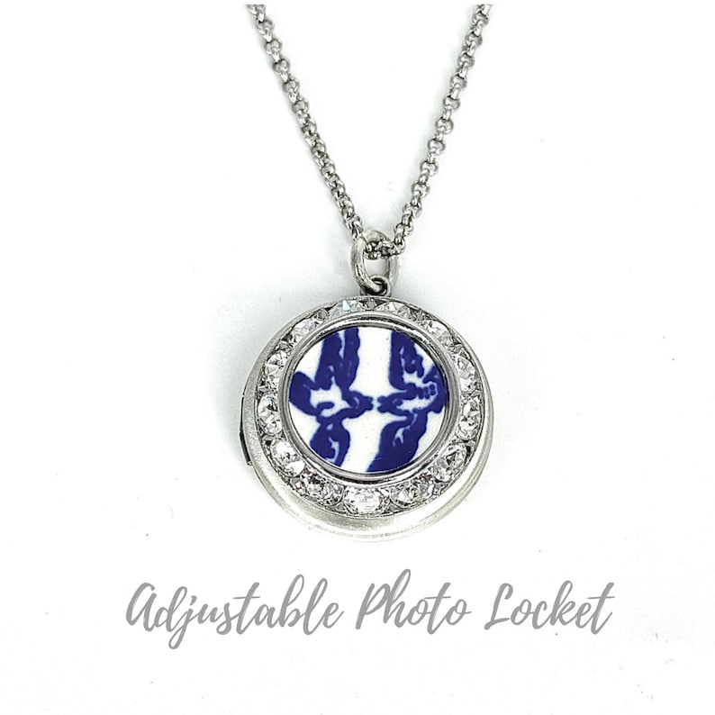 May include: A silver-coloured adjustable photo locket necklace. The round pendant has a blue and white design, encircled by clear crystals. The necklace features a delicate chain.