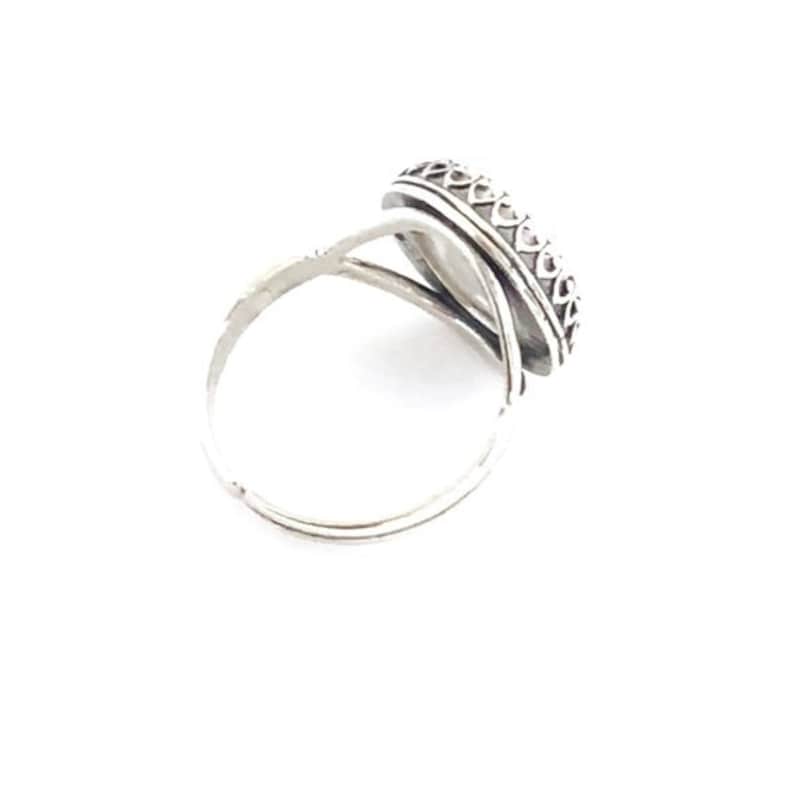 Pu&ograve; includere: Un anello d'argento con una pietra ovale di colore chiaro. L'anello presenta una fascia decorativa attorno alla pietra e una fascia semplice ed elegante. L'anello &egrave; posto su uno sfondo bianco, evidenziando il suo design e la sua maestria.