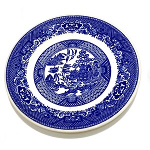 May include: A round, white and blue ceramic plate with a detailed Willow pattern. The plate features a central scene of a bridge, pagoda, and birds, surrounded by a geometric and floral border. The plate is approximately 25 cm in diameter.