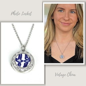 May include: A silver photo locket necklace with a round pendant featuring a blue and white floral design. The pendant is surrounded by clear crystals. The image includes the words "Photo Locket" and "Vintage China".