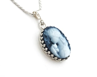 May include: Silver-toned necklace featuring an oval cameo pendant. The pendant showcases a blue and white profile of a woman, set within a decorative silver frame. The necklace has a delicate chain.