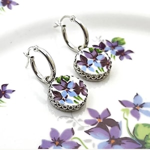 Peut inclure: Une paire de boucles d'oreilles cr&eacute;oles en argent avec des breloques rondes blanches orn&eacute;es d'un motif floral de violettes violettes et bleues. Chaque breloque est ench&acirc;ss&eacute;e dans un serti en argent festonn&eacute;, suspendue &agrave; un anneau.