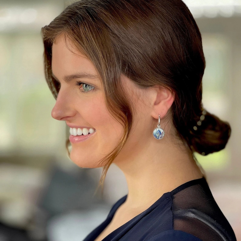 Peut inclure: Une boucle d'oreille pendante circulaire avec une incrustation en c&eacute;ramique &agrave; motifs bleus et blancs, sertie dans un cadre en m&eacute;tal argent&eacute;. La boucle est suspendue &agrave; un petit anneau argent&eacute; poli qui se fixe au lobe de l'oreille.
