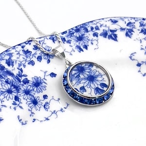 May include: A silver necklace with a blue and white floral pendant surrounded by blue crystals.