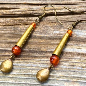 May include: A pair of handcrafted earrings featuring a brass tube design with orange-red beads and teardrop-shaped pendants. The earrings have a vintage, bohemian aesthetic, perfect for adding a unique touch to any outfit.