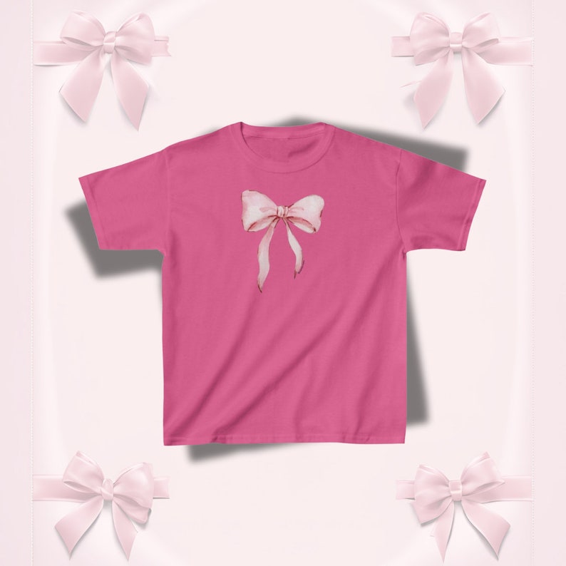 Pu&ograve; includere: Una maglietta rosa acceso con un disegno di fiocco ad acquerello. Il fiocco &egrave; rosa chiaro con sfumature delicate e nastri lunghi e fluenti. La maglietta &egrave; di colore pieno, con girocollo classico e maniche corte. Lo sfondo presenta fiocchi rosa decorativi.