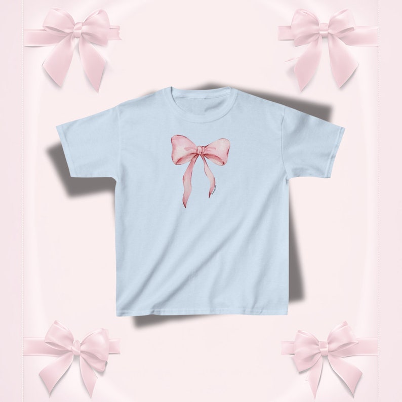 Pu&ograve; includere: T-shirt azzurra con un motivo a fiocco rosa acquerellato. Il fiocco, con lunghi nastri fluttuanti, &egrave; centrato sul davanti. La maglietta &egrave; in stile girocollo classico.