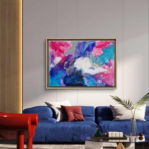 Könnte beinhalten: Abstraktes Gemälde in den Farben Pink, Blau, Lila und Weiß. Das Gemälde ist in einem hellen Holzrahmen gerahmt und hängt an einer weißen Wand über einem blauen Sofa.