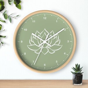 May include: A green clock with a white lotus flower design and white numbers. The clock hands are white and the clock is made of wood.