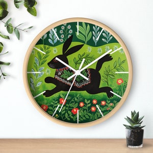 May include: A round wooden clock with a black rabbit running through a green and red floral design. The rabbit is wearing a colorful patterned collar.