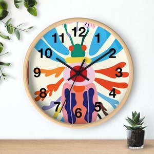 May include: A colorful clock with a whimsical design featuring a stylized insect with a red eye and blue, orange, and green accents. The clock face has black numbers and hands.