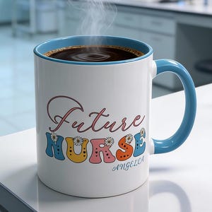 May include: A white ceramic mug with a blue interior and handle, filled with dark liquid and steam. The mug features the words "Future Nurse" in colorful, retro-style lettering. The mug is on a white surface in a laboratory setting.